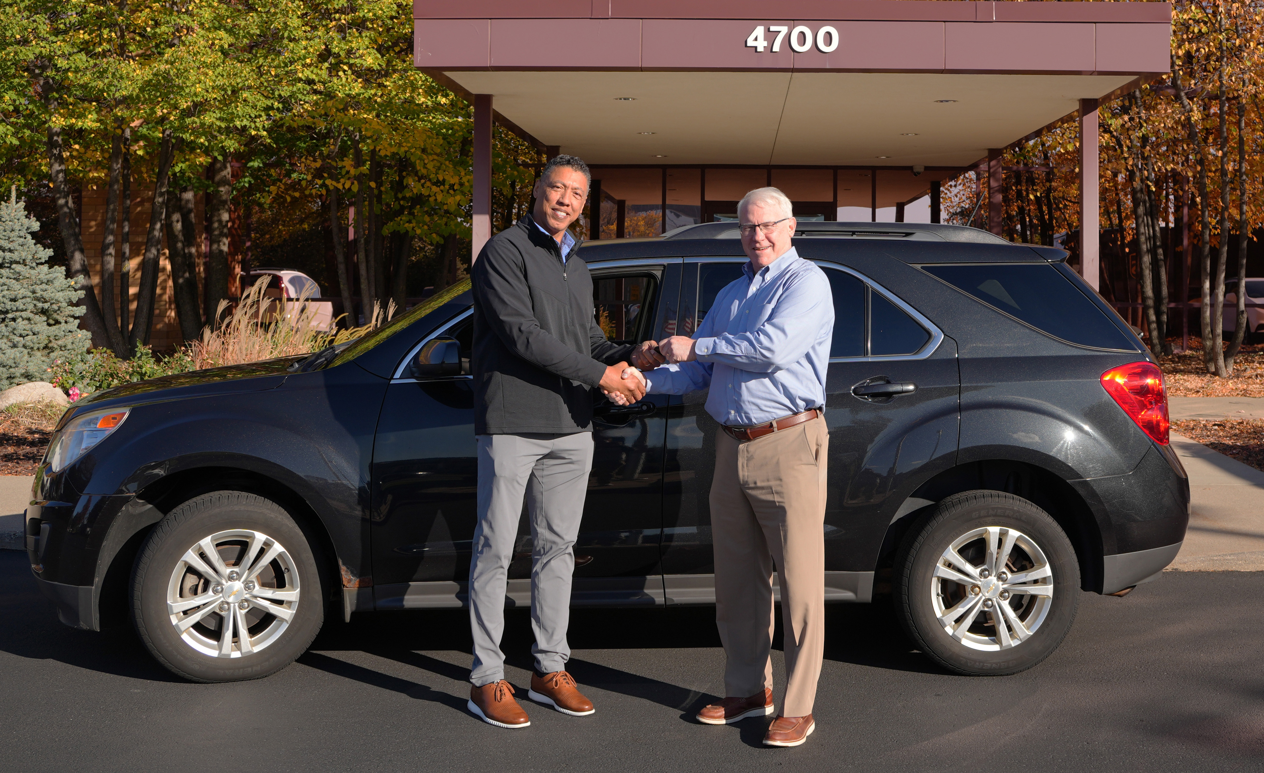 Western National employee shaking hands with member of the Minnesota Commerce Fraud Bureau in fron of donated vehicle.